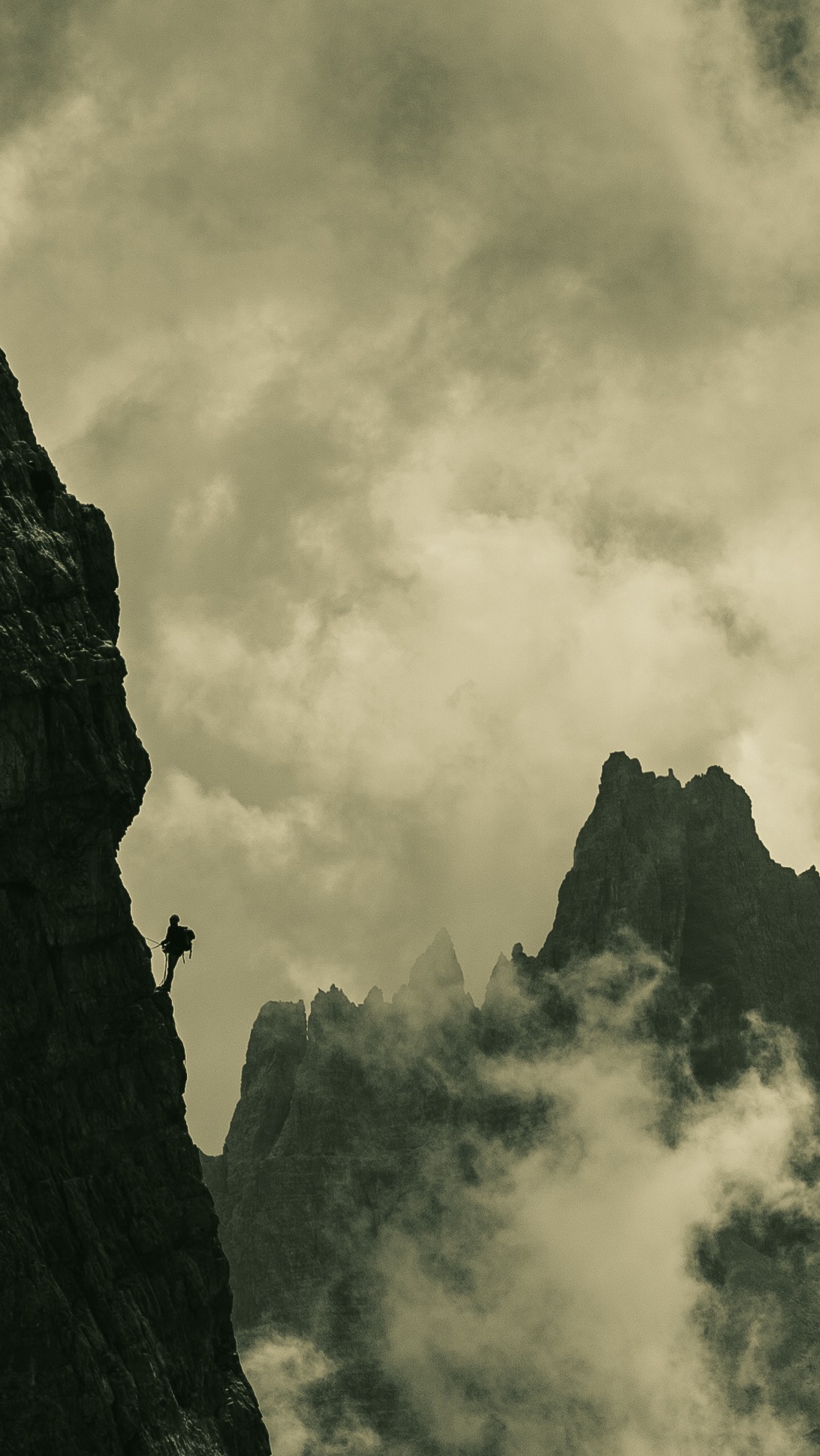 Man climbing a mountain in sepia tones, silhouette against the sky